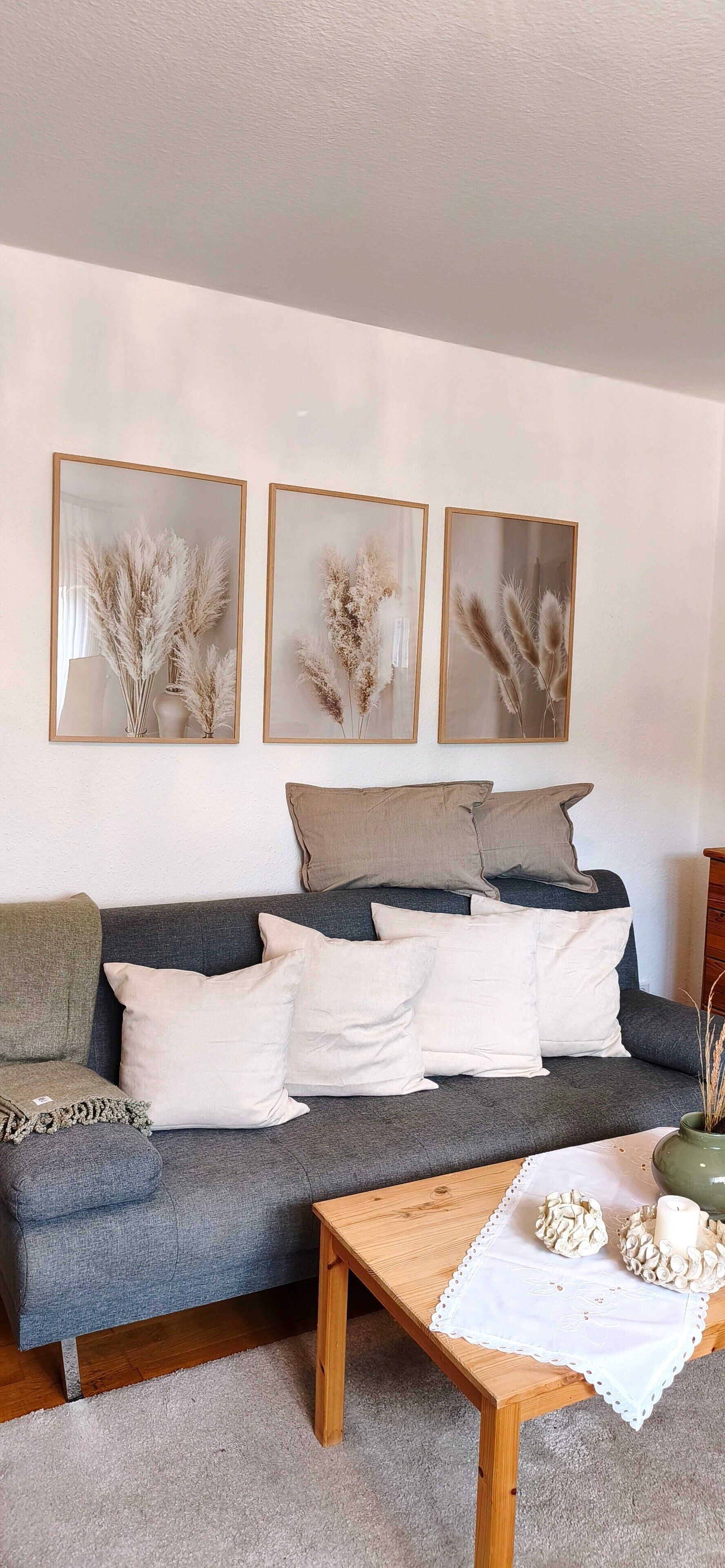 A living room with a grey sofa, white and grey cushions, a wooden coffee table, and three framed wall art pieces.