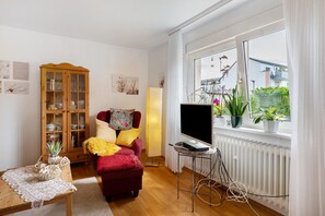 A living room with a red sofa, wooden cabinet, TV, and potted plants by a window.