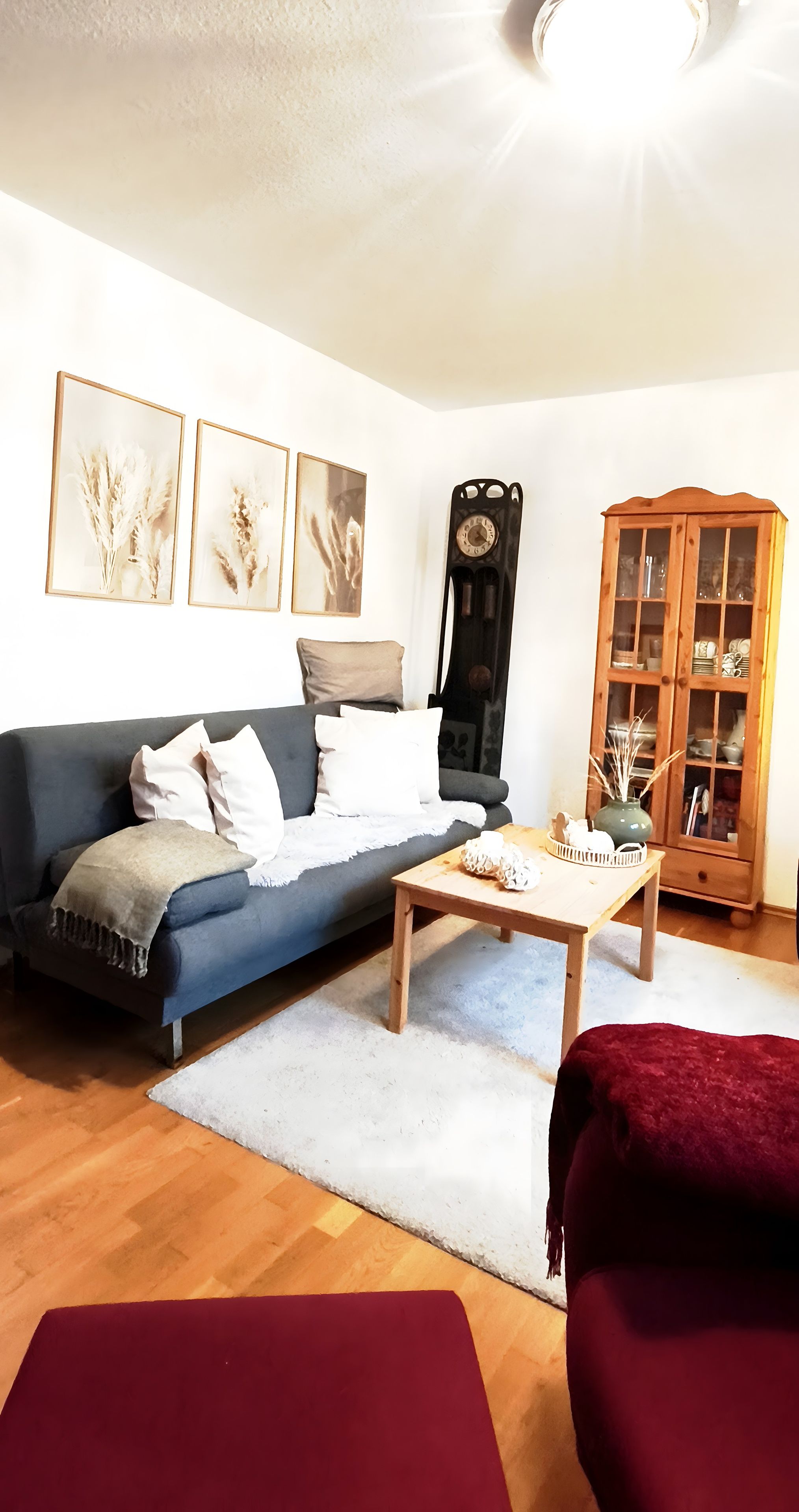 A living room with a blue sofa, a wooden coffee table, a red chair, and a cabinet with glass doors.