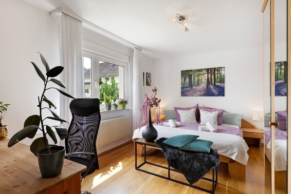 A modern bedroom with a bed, bedside tables, a chair, a potted plant, and a window with curtains.