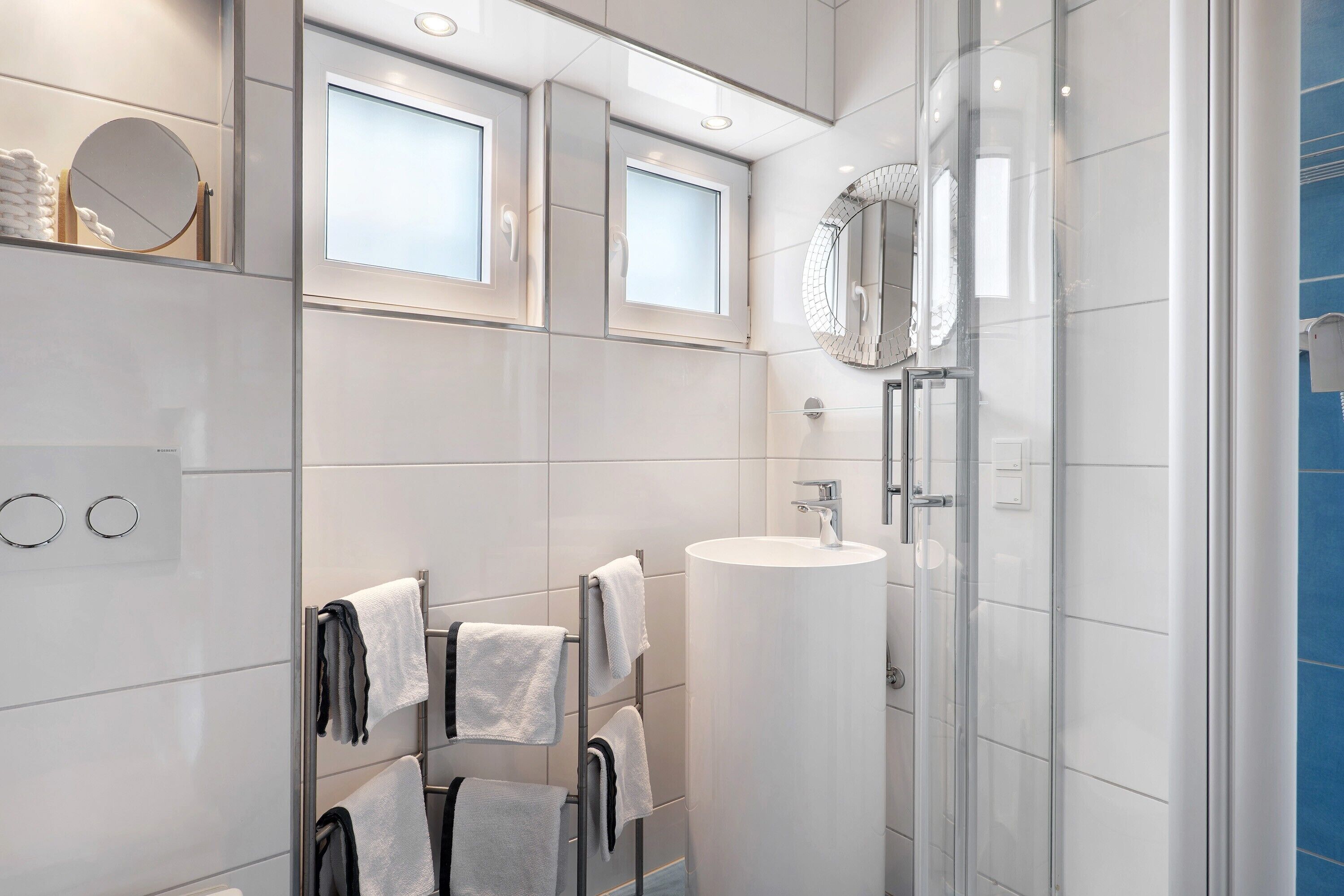 A modern bathroom with a glass shower enclosure, a white sink, and a towel rack with multiple towels.