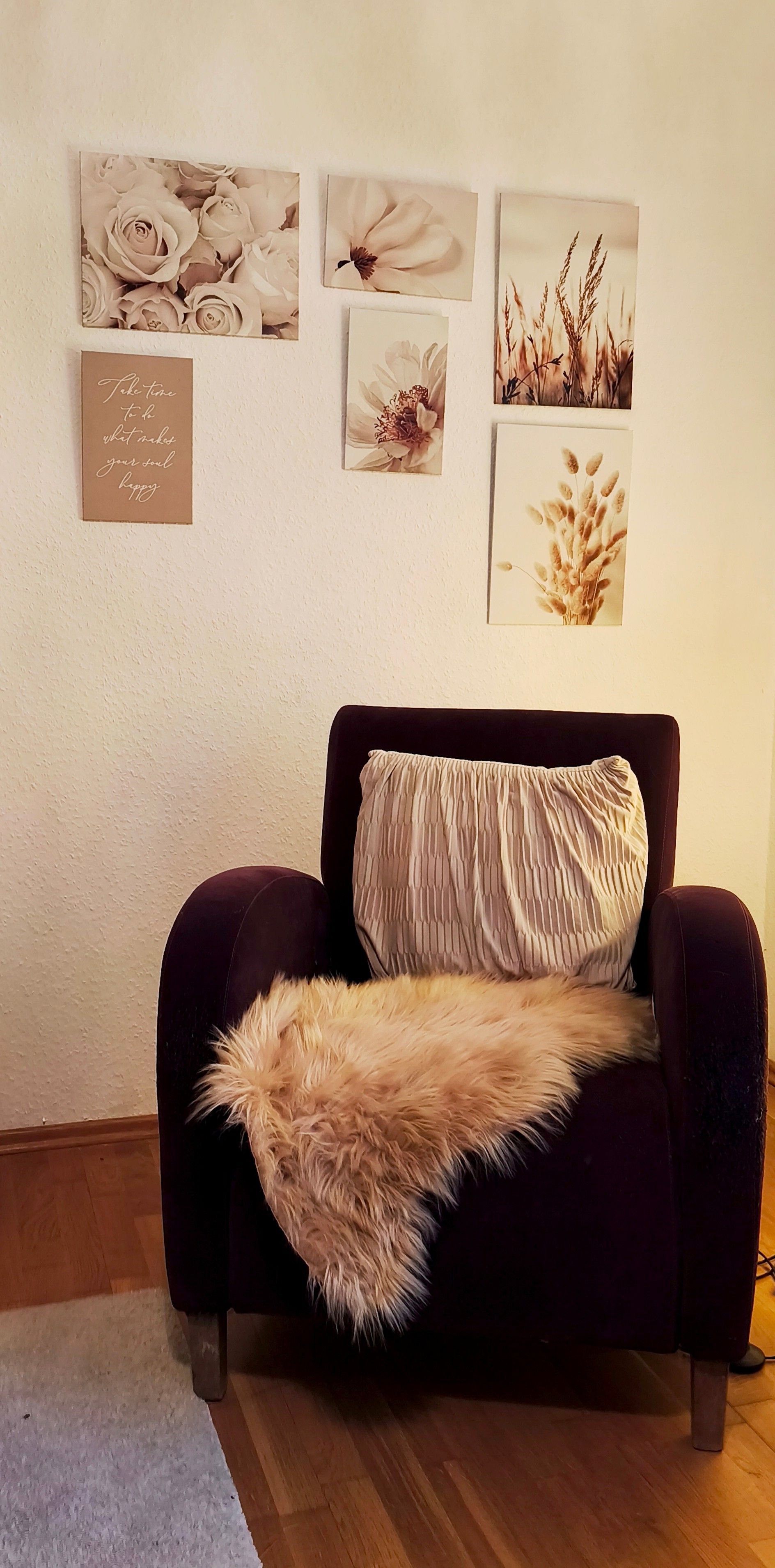 Una habitación con un sofá de color oscuro, una manta suave y un cuadro floral colgado en la pared.