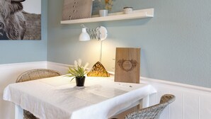 Ein Essbereich mit Tisch für zwei Personen, einem Blumentopf, einer Wandlampe und einem Regal mit Dekoration.