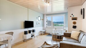 Ein Wohnzimmer mit Fernseher, Sofa und Blick durch ein Fenster.