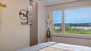 Ein Schlafzimmer mit einem Bett, einem Fenster mit Landschaftsblick, einer Wand mit einem runden Schild und einem Traumfänger.