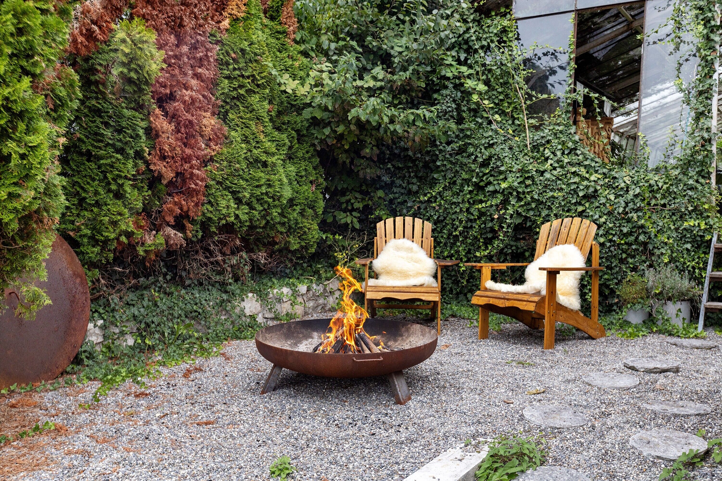 A fire pit with chairs, surrounded by gravel and greenery.