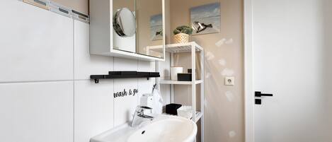 A bathroom with a white sink, mirror, and shelves with toiletries.