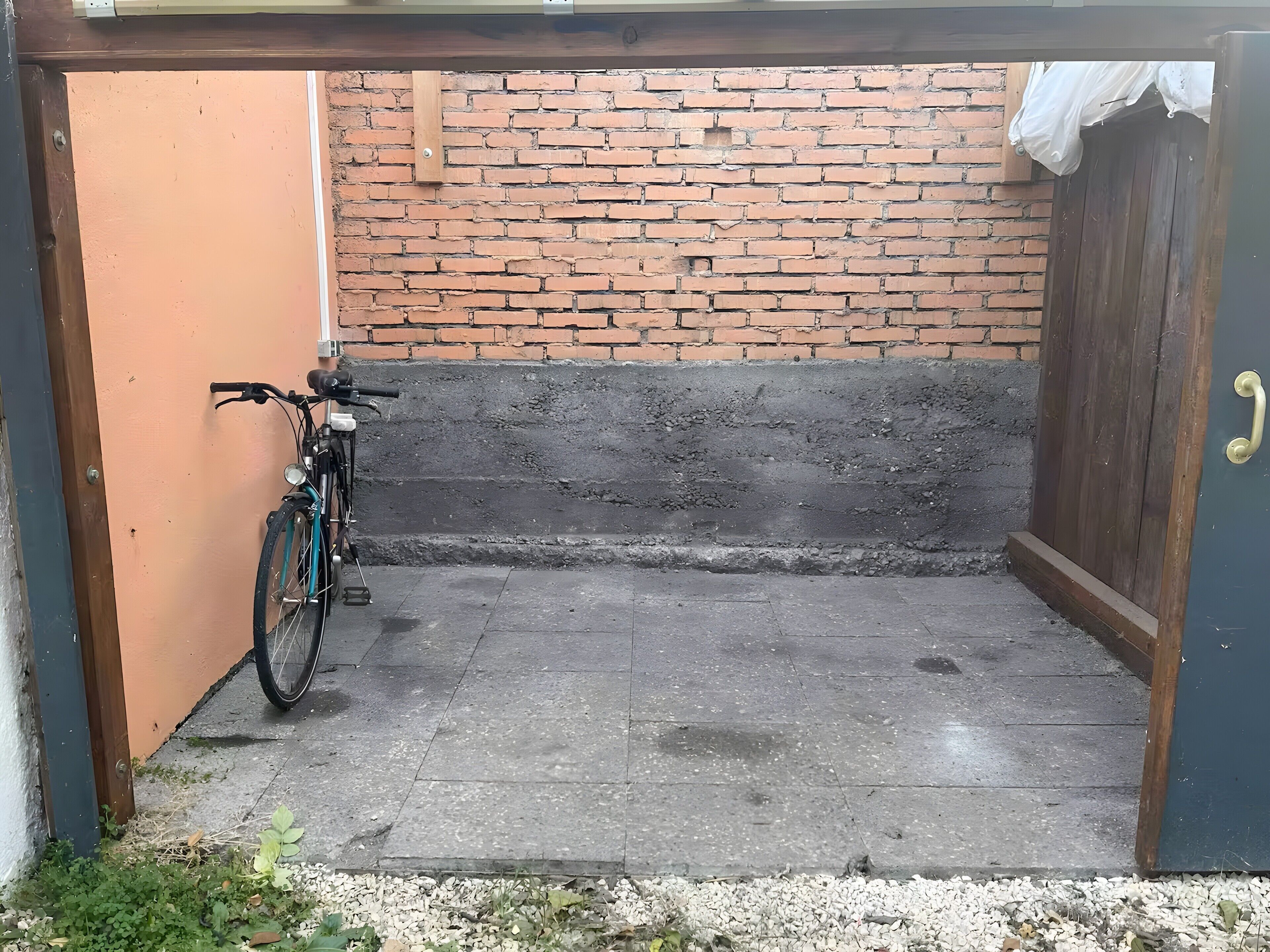 Een smalle buitenruimte met een bakstenen muur, een houten deur en een fiets die tegen de muur staat.