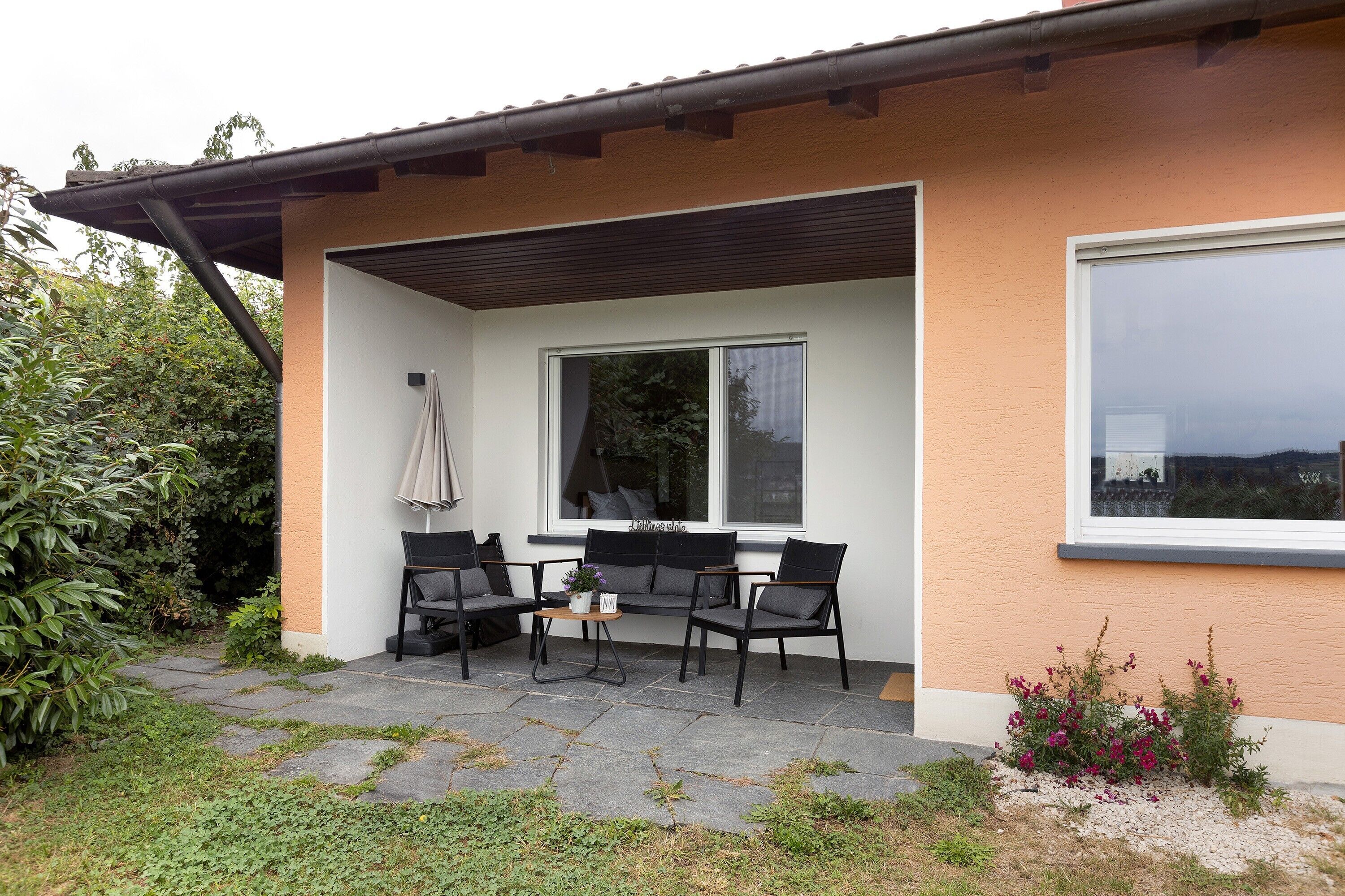 Ein modernes Gebäude mit einer Terrassenfläche, Sitzgelegenheiten im Freien und einem großen Fenster.