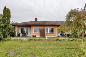 A two-story house with a tiled roof, a satellite dish, and a small garden with a lawn and a tree.