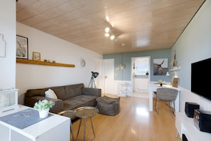 A living room with a brown sofa, a white coffee table, a small round table, and a television.