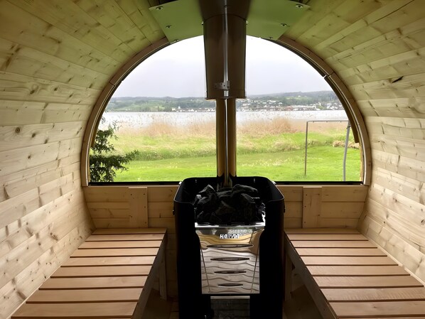 A wooden interior with a large arched window, a fireplace, and a view of a lake and fields.