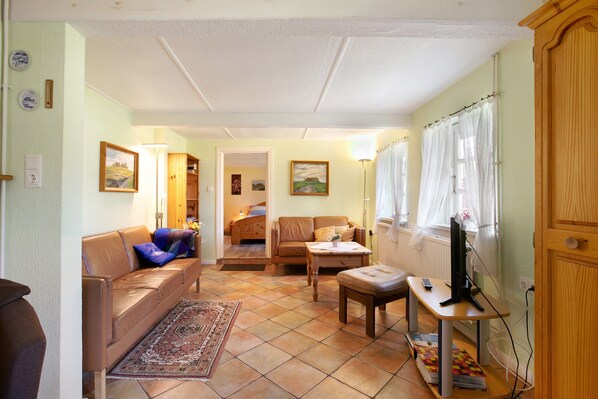 Una sala de estar con un sofá, una mesa de centro, un televisor sobre un mueble, una ventana con cortinas y una puerta.