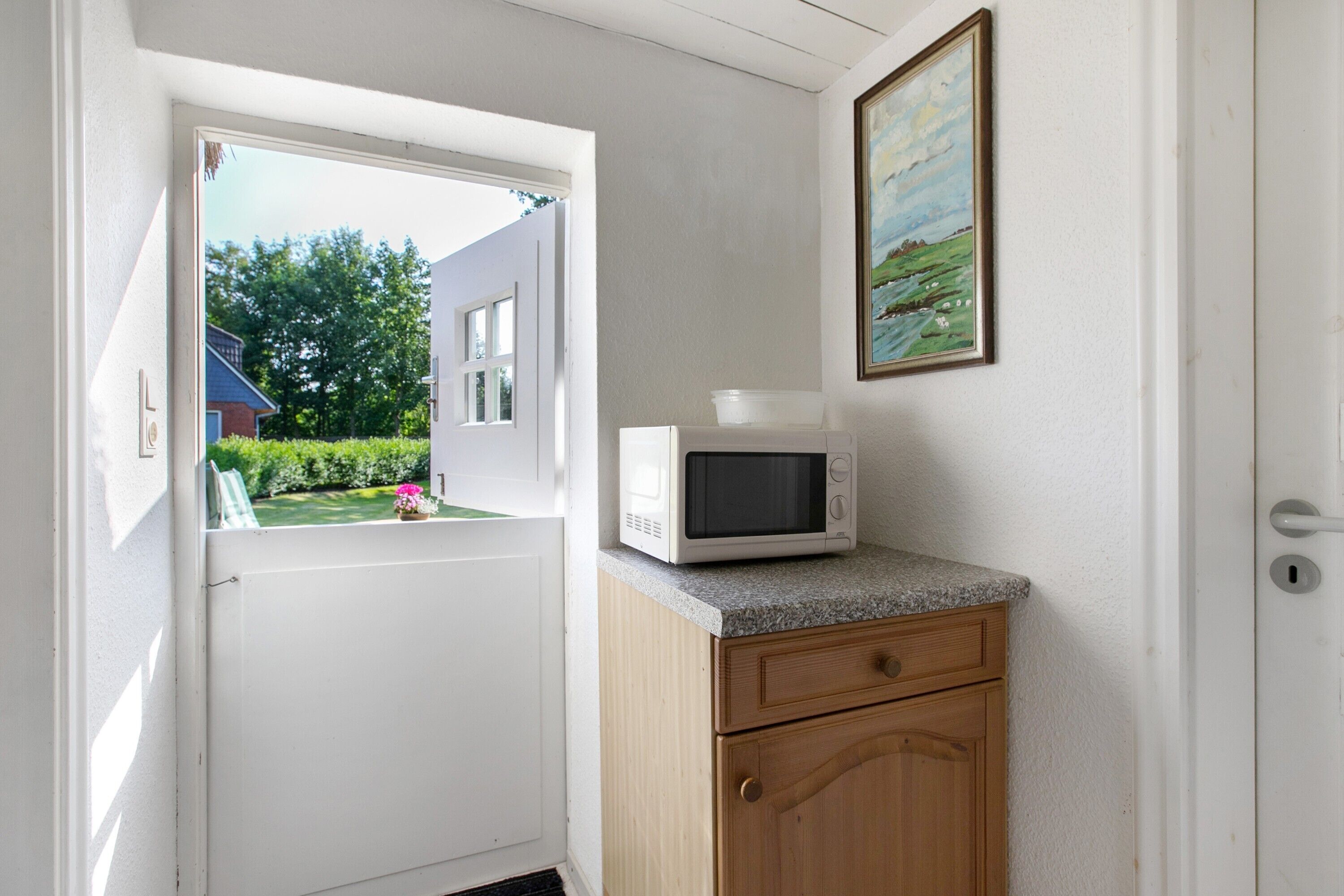 A kitchen with a microwave on a countertop, a wooden cabinet, and a door leading to a garden.