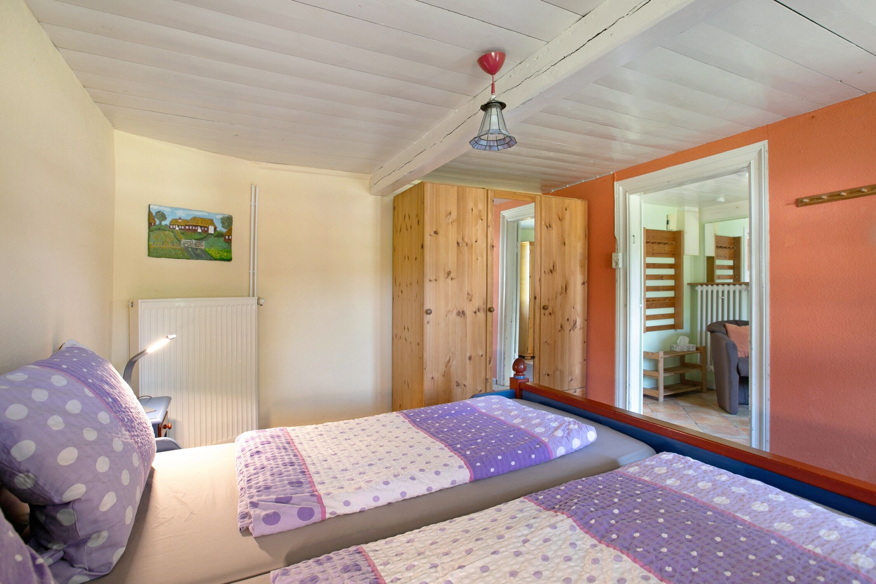 Un dormitorio con dos camas, ventilador de techo, radiador y un cuadro en la pared.