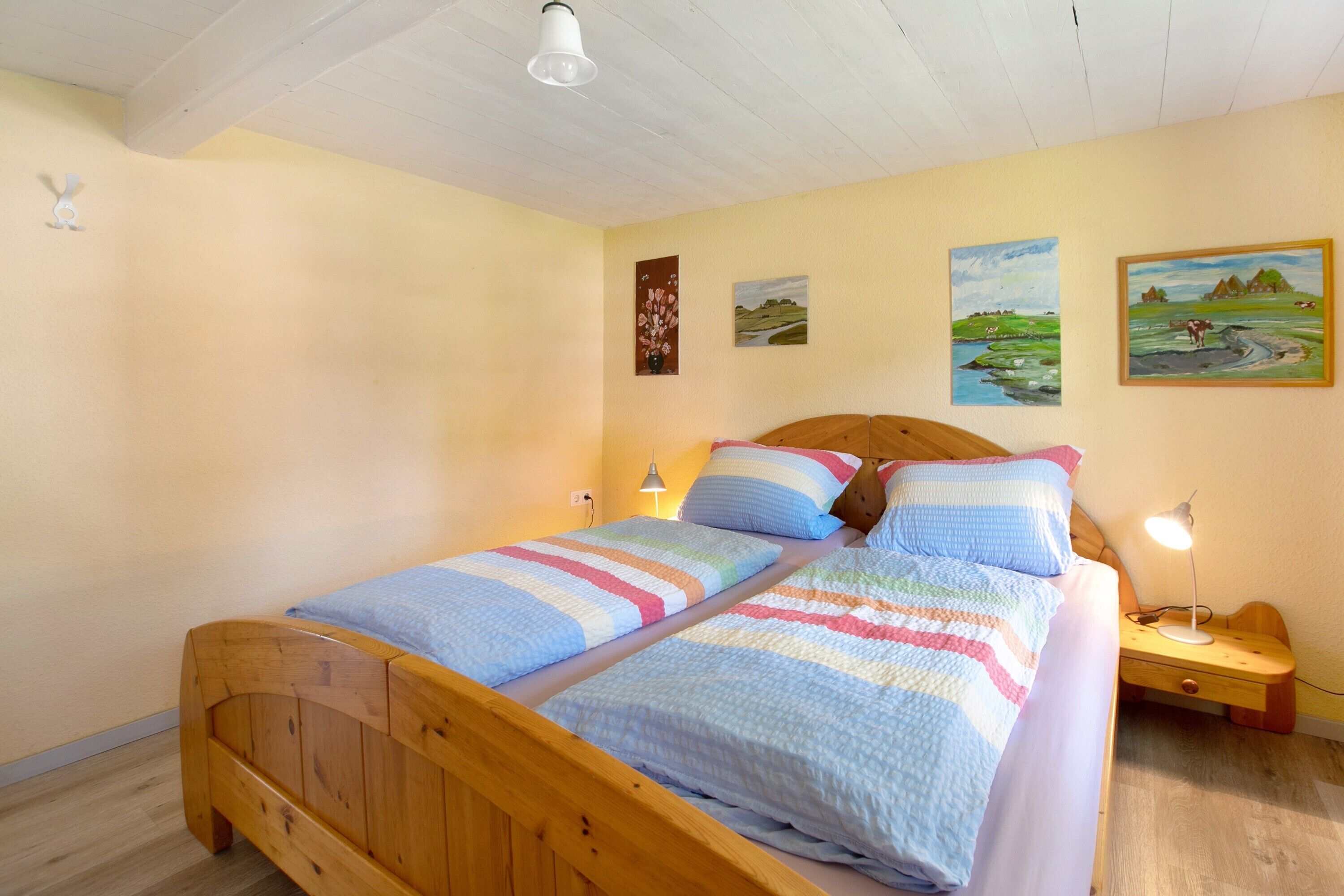 A double bed with striped bedding, a wooden headboard, bedside tables with lamps, and three landscape paintings on the wall.