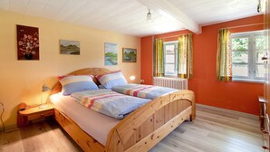 Een houten bed met een sprei, een nachtkastje met een lamp, en een raam met gordijnen.