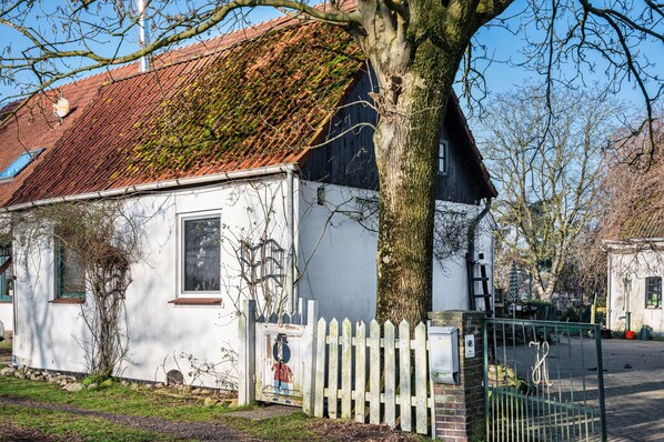 Ein weißes Gebäude mit rotem Dach, weißem Zaun und einem Baum davor.