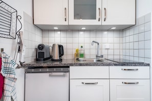 A kitchen with white cabinets, a granite countertop, a coffee maker, a kettle, a sink, and a dish rack. - Holiday Home 'Harmonie Tiny House' (Oyten)