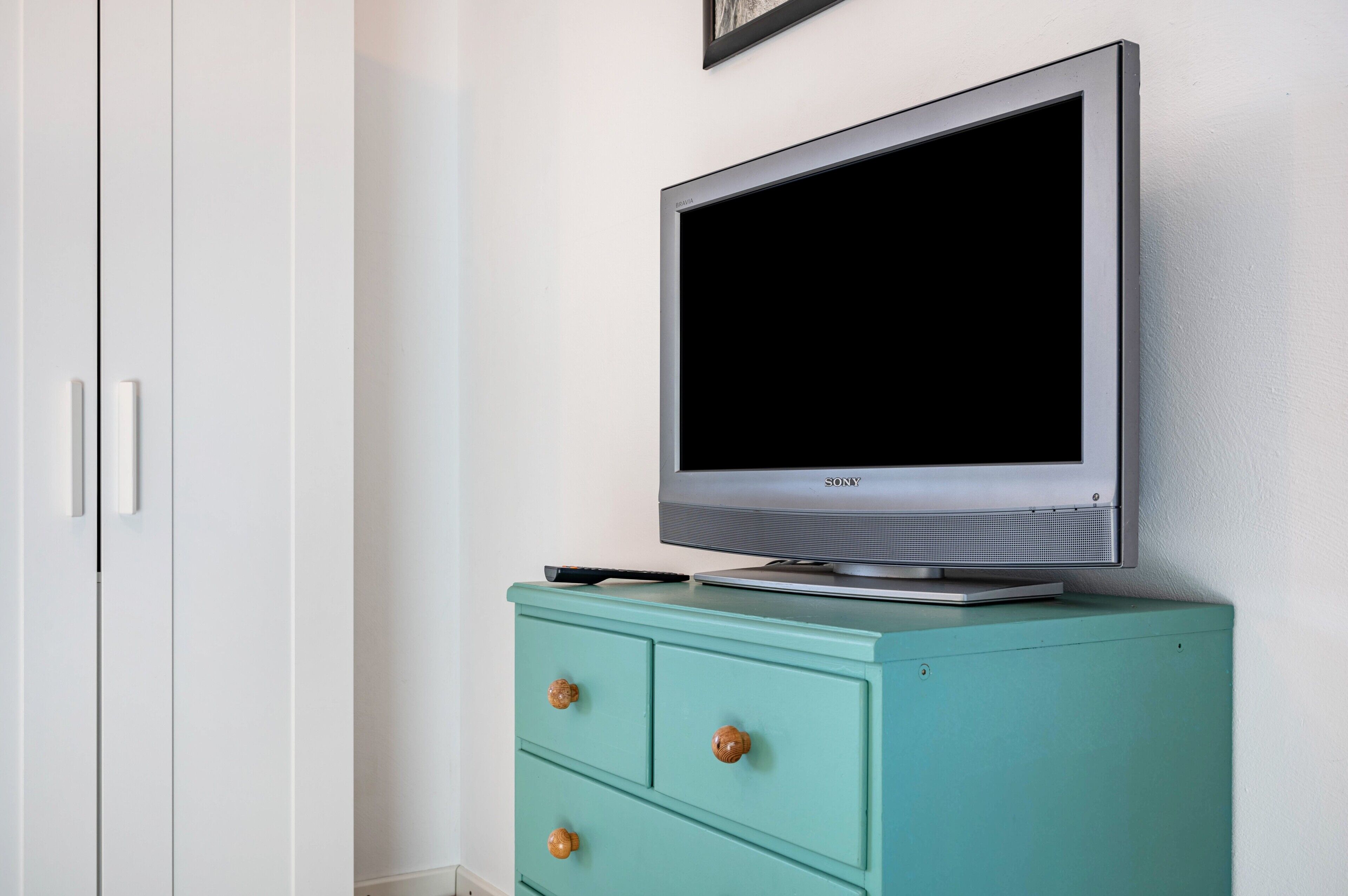 Een televisie op een groen kastje, een witte kledingkast en een lijst met een afbeelding aan de muur.