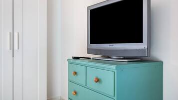 Een televisie op een groen kastje, een witte kledingkast en een lijst met een afbeelding aan de muur.