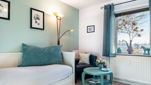 Una habitación con cama, una mesita de noche con un florero, un radiador y una ventana con vistas a árboles.