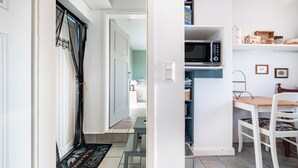 Una cocina con microondas, estantes y una zona de comedor con una silla y mesa.