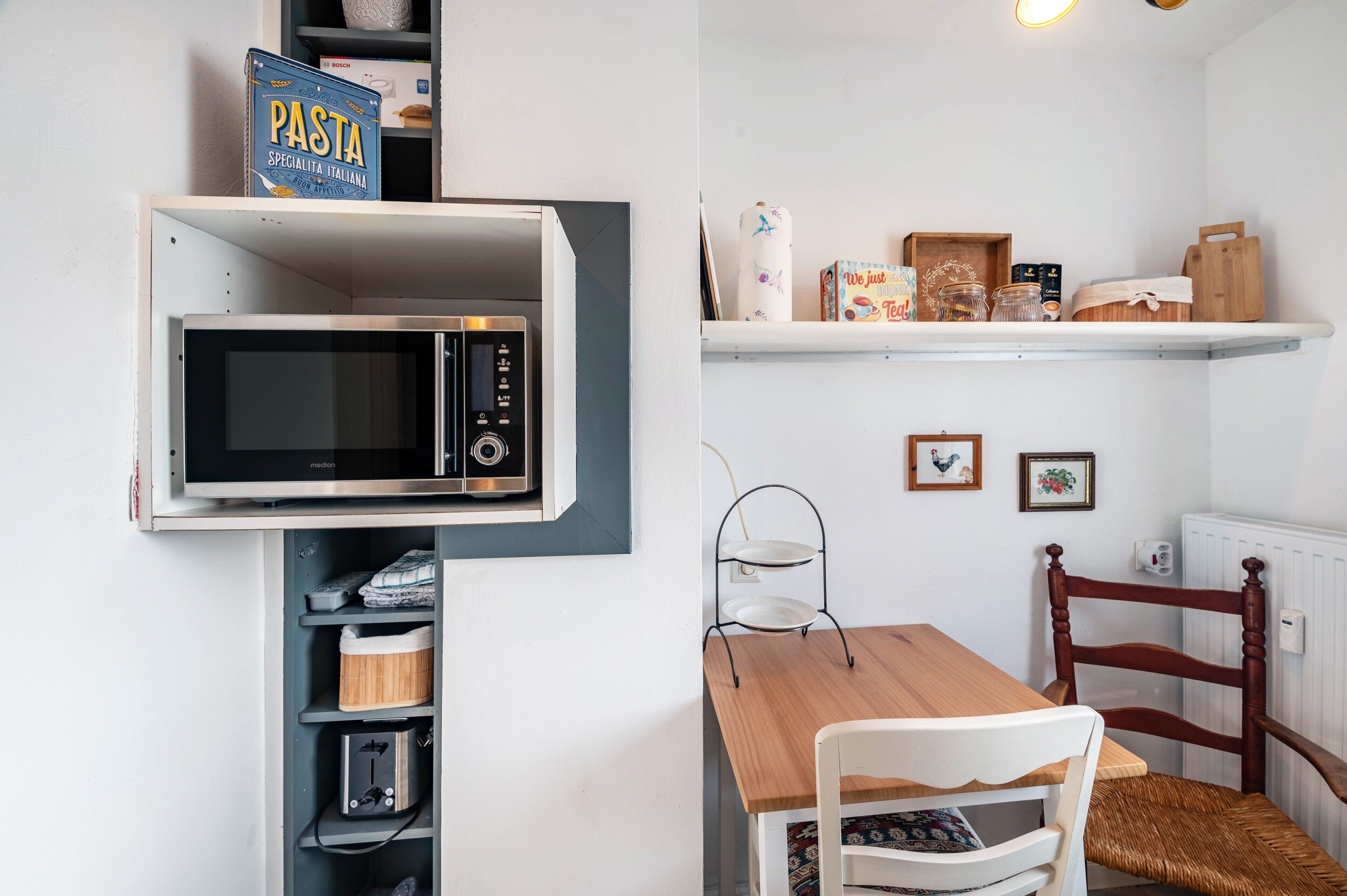 A kitchen with a microwave, a shelf with pasta, and a dining table with chairs.