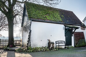 A white building with a moss-covered roof, a wooden bench, and a tree in the foreground. - Holiday Home 'Harmonie Tiny House' (Oyten)