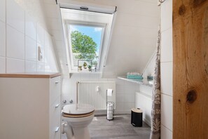 Une salle de bain moderne équipée de toilettes, d’un radiateur, d’une fenêtre donnant sur des arbres et d’une porte en bois.