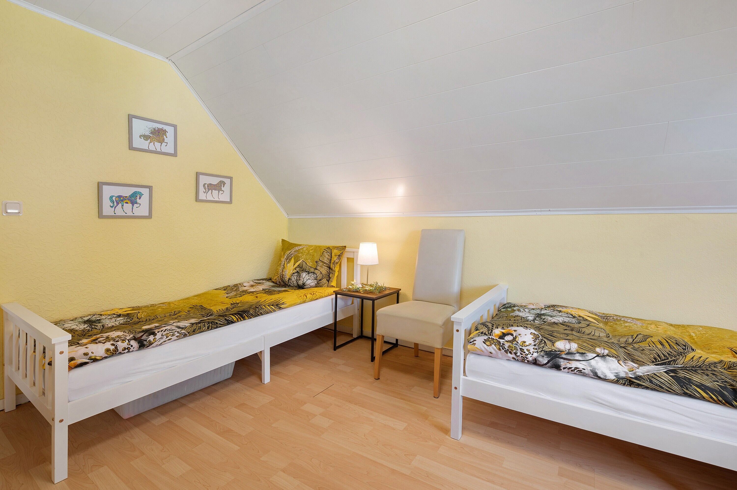 Un dormitorio con dos camas individuales, una mesita pequeña, una silla y tres cuadros en la pared.