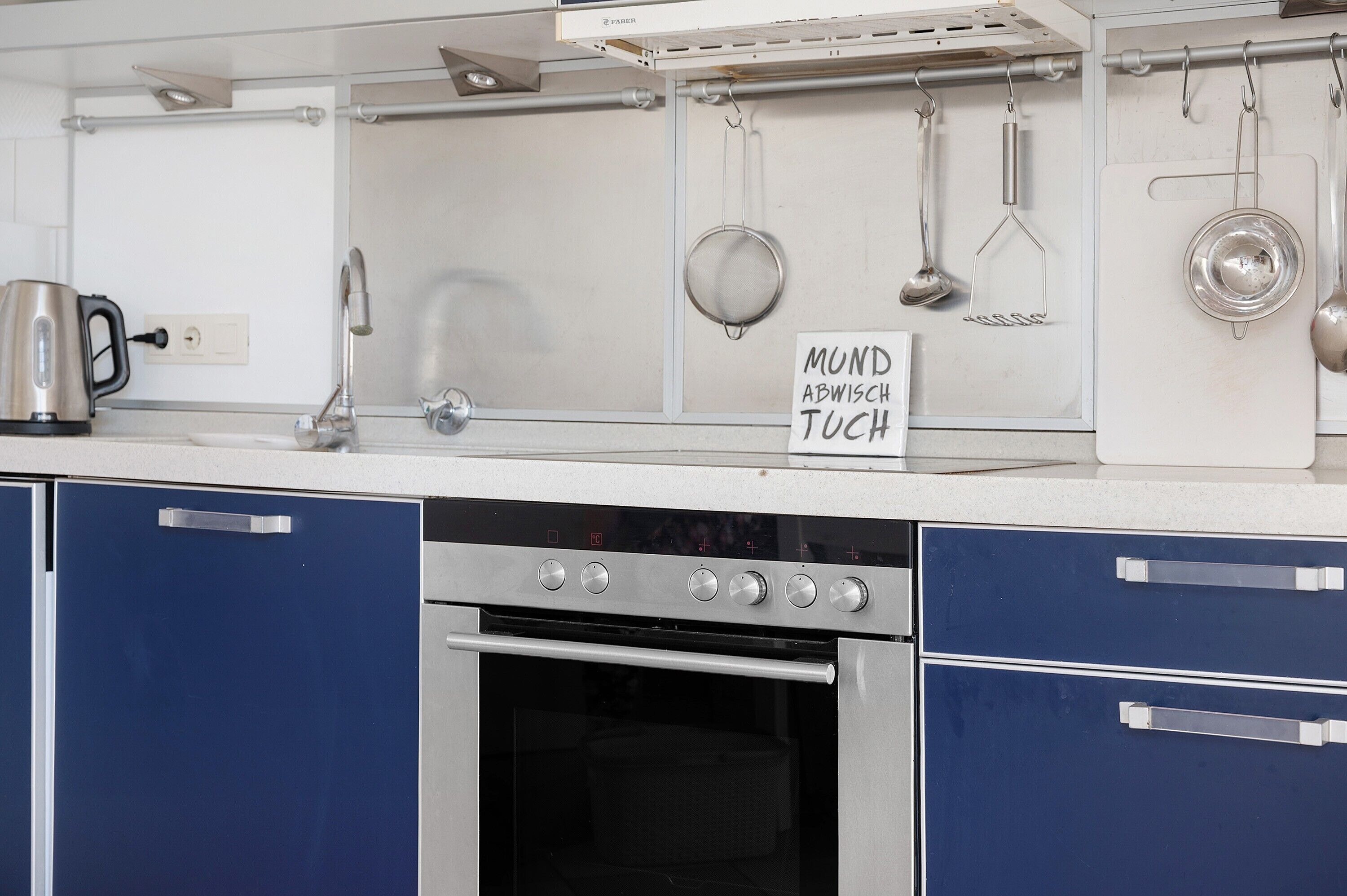 A kitchen with a stainless steel range hood, a kettle, and hanging utensils.