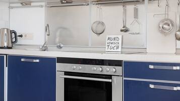 A kitchen with a stainless steel range hood, a kettle, and hanging utensils.