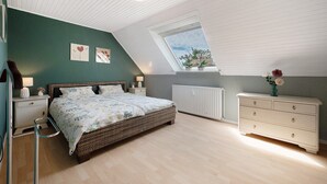 A bedroom with a sloped ceiling, a bed, a dresser, a nightstand, a window, and a radiator.