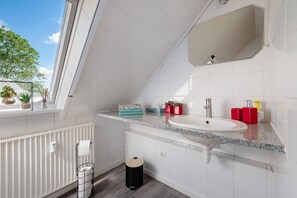 A modern bathroom with a skylight, white tiles, a granite countertop, a sink, and a window with plants.