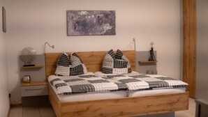 A modern bedroom with a wooden bed, two bedside tables, a wall-mounted lamp, and a piece of abstract art. - Apartment 'Ferienwohnung Haus Biggi' with Private Terrace, Private Garden and Wi-Fi (Gransdorf)
