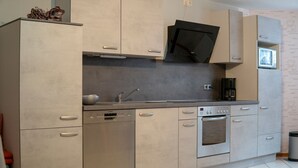 A modern kitchen with stainless steel appliances, a dishwasher, and a built-in oven. - Apartment 'Ferienwohnung Haus Biggi' with Private Terrace, Private Garden and Wi-Fi (Gransdorf)