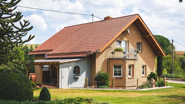 A two-story house with a red-tiled roof, a balcony with hanging plants, and a small porch area. - Apartment 'Ferienwohnung Haus Biggi' with Private Terrace, Private Garden and Wi-Fi (Gransdorf)