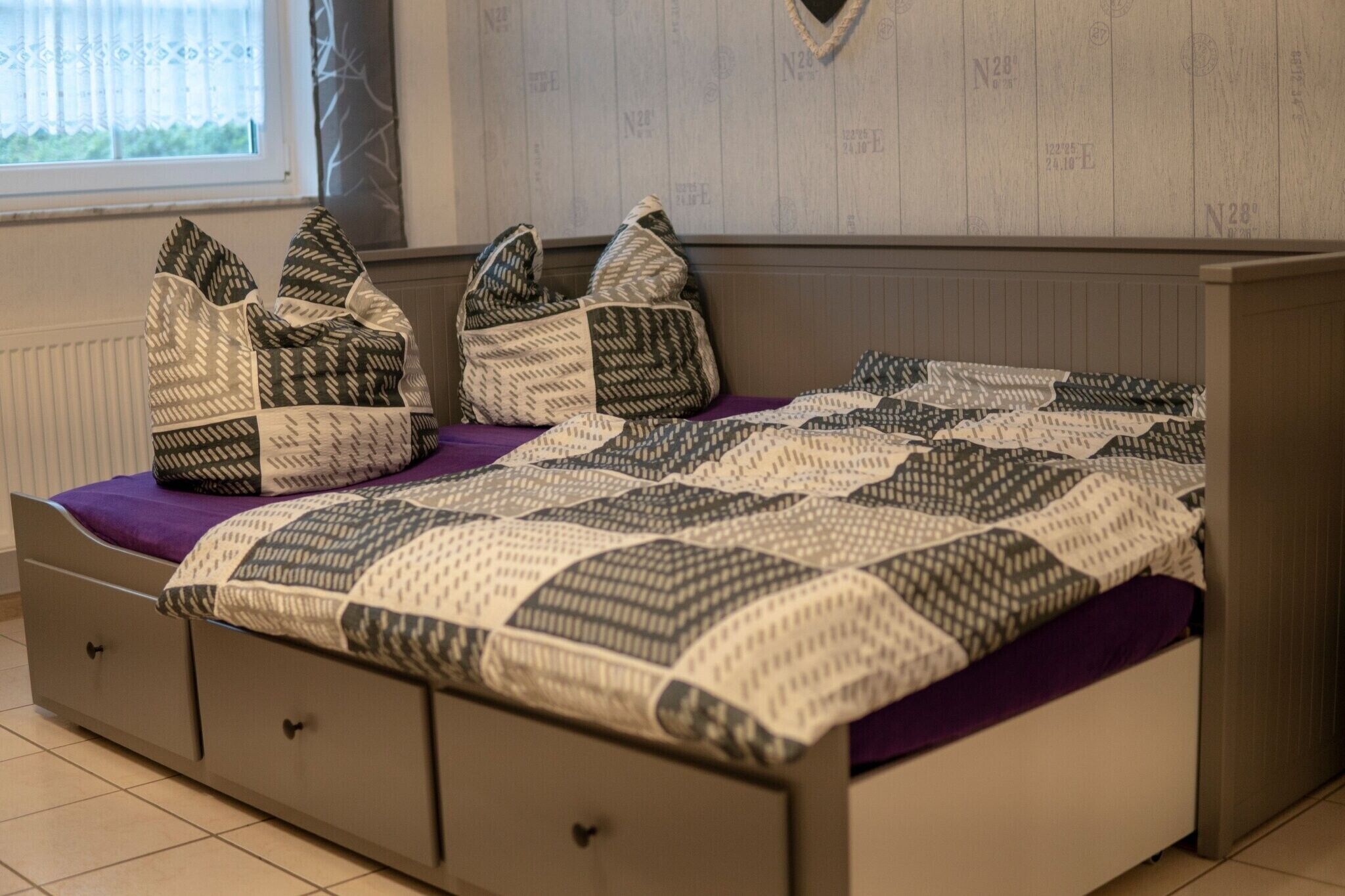 Un lit avec une couette à motifs, deux oreillers et un plaid violet.