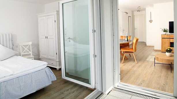 A bedroom with a bed, a wardrobe, and a sliding glass door leading to a dining area with a table and chairs.