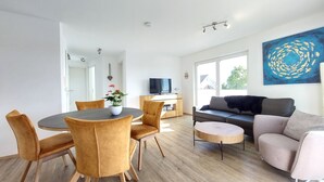 A modern living room with a dining area, a sofa, a television, and a large window.