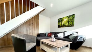 Ein modernes Wohnzimmer mit Treppe, einer Sofagarnitur, einem Couchtisch und einem Wandbild mit Waldmotiv.