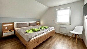 Ein Schlafzimmer mit einem hölzernen Bett, einem Nachttisch, einem Sessel, einem Fenster und einer Deckenleuchte.