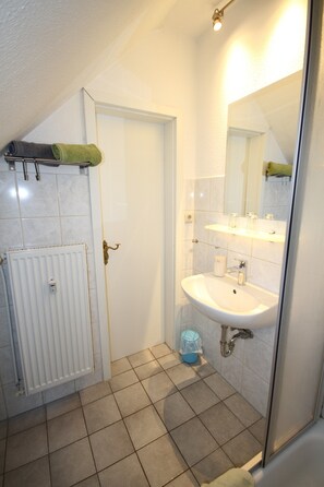 Ein Badezimmer mit weißem Waschbecken, einem Spiegel, einem Handtuchhalter und einer Duschkabine.