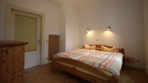 Een slaapkamer met een houten bed, een deur en een klein houten kastje.