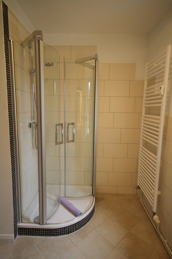 A glass-enclosed shower with a curved design, a white tiled floor, and a white radiator on the wall. - Villa 'Ferienwohnung Charlotte' with Shared Terrace, Shared Garden and Wi-Fi (Schierke)