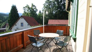 Een houten terras met een ronde tafel en vier stoelen, omgeven door een houten hekwerk.