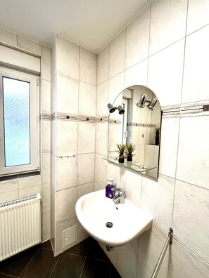 Un bagno con lavandino bianco, specchio, finestra e termosifone.