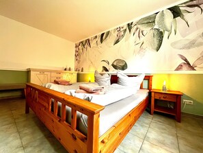 Una camera da letto con un letto di legno, un comodino, una lampada a parete e una decorazione floreale al muro.