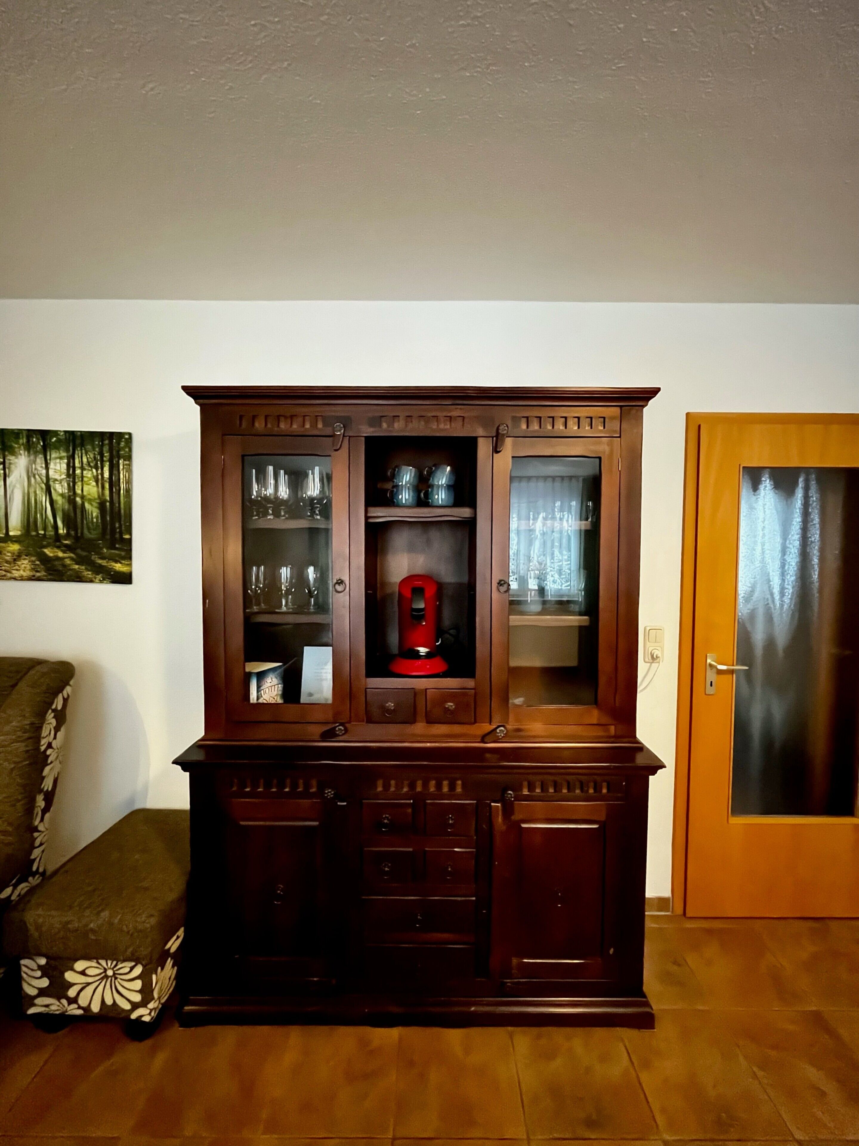 A wooden cabinet with glass doors, a red appliance, and a door with a frosted glass panel.